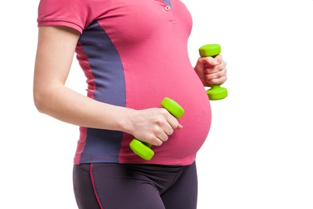 Happy pregnant mom in sportsuit exercising with dumbbells over white backgroundの写真素材