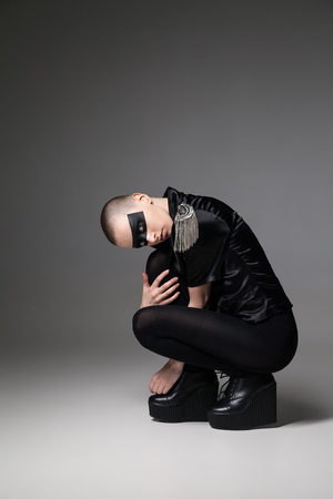 agressive beautiful bald sitting woman  with mask makeup posing on backgroundの写真素材