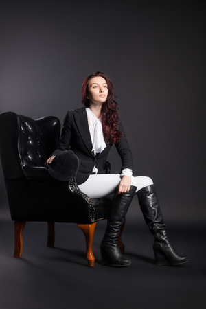 Classical waist portrait of a young female horse rider black armchair over dark backgroundの写真素材