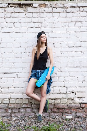 Young beautiful sexy girl in denim shorts poses to the camera with her skateboard over white brick wall.の写真素材