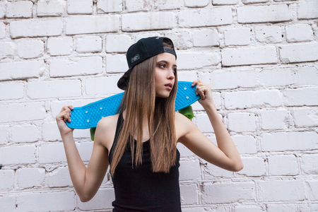 Young beautiful sexy girl in denim shorts poses to the camera with her skateboard over white brick wall.の写真素材