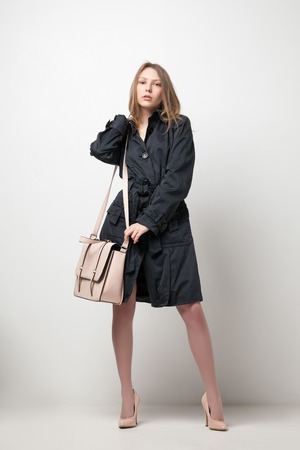 Fashion portrait of a young beautiful girl in long black coat with bagの写真素材