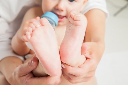Mother holds feet of newborn son with baby bottle over white backgroundの写真素材