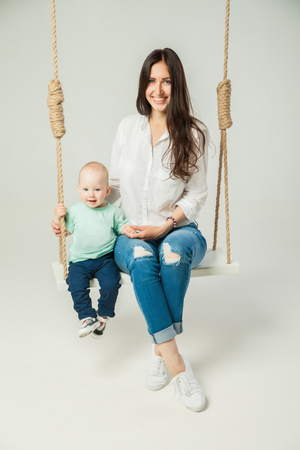 Young woman with little son sitting on swing over white backgroundの写真素材