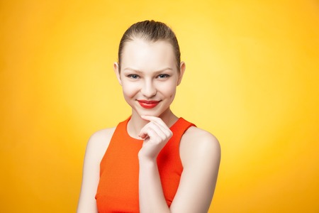 Portrait of an attractive fashionable young  woman in orange dress on yellow backgroundの写真素材