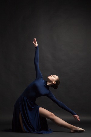 Posing dancer in long deep blue dress over dark backgroundの写真素材