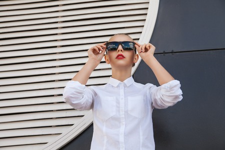 Woman in sunglasses looking up against of building wallの写真素材