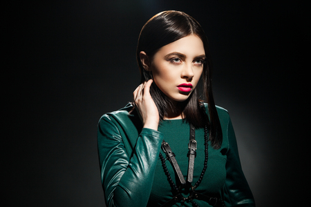 Portrait of dark-haired model in green dress with black belt and make-up looking awayの写真素材