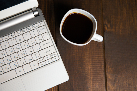 Close-up of black coffee in cup near keyboard on wooden backgroundの写真素材