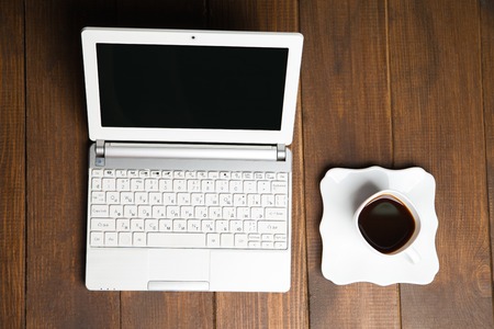 View on laptop with cup of black coffee on saucer.Wooden background.From aboveの写真素材