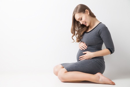 Beautiful young pregnant woman sitting and looking at her belly.Studio shotの写真素材