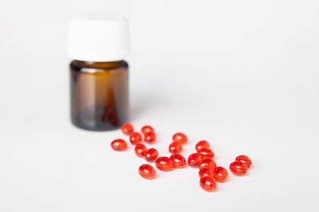 close-up of red pills on white surface with closed bottle on backgroundの写真素材