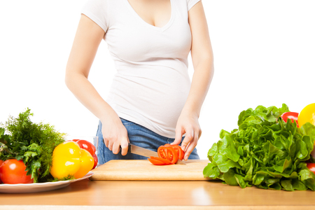 Pregnant woman cuts tomato on board in close-upの写真素材