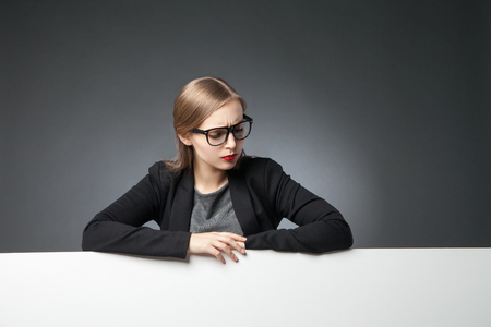 portrait of sad young woman with red lips in jacket and glasses looking downの写真素材