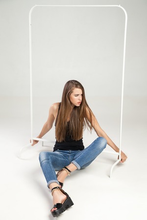Portrait of angry young model leaning on empty clothes rack.Studio shotの写真素材
