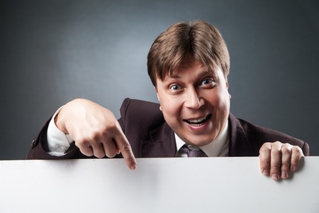 Portrait of smiling adult businessman pointing at blank space with index finger.Studio shotの写真素材