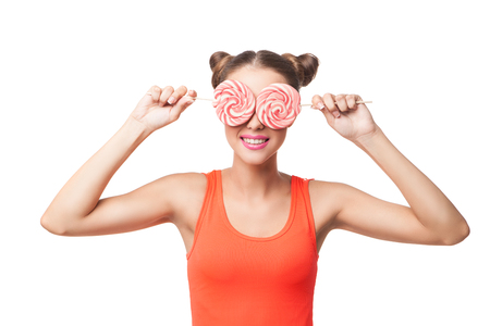 Portrait of smiling young woman in orange top covering eyes with candies.Isolatedの写真素材