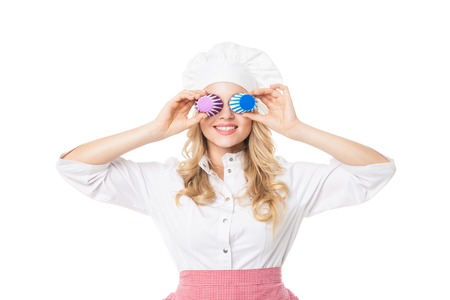 Portrait of smiling blonde woman covering eyes with cupcake baking forms.Studio shot.Isolated.の写真素材