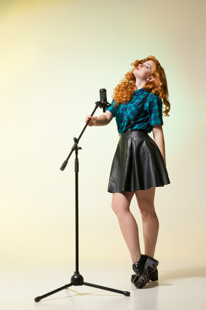 Beautiful young singer with eyes closed holding mic.Studio shotの写真素材