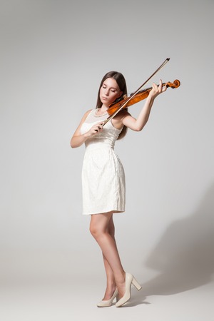 Portrait of beautiful young woman in white dress playing violin.Studio shotの写真素材