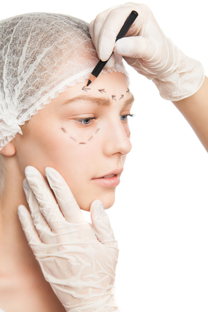 Close-up of plastic surgeon in gloves drawing contour on patients faceの写真素材