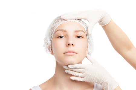 Portrait of young woman in medical hat looking at camera while doctor touches her face.Isolatedの写真素材