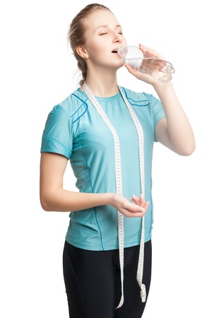 Beautiful  female fitness model holding a bottle of water, wearing tape measure. Isolated on whiteの写真素材