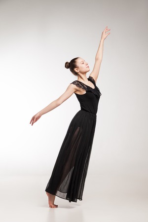 Young ballet dancer wearing black transparent dress dancing over white backgroundの写真素材