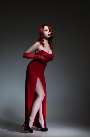 Beautiful young Woman with red hair dressed in red elegant dressの写真素材