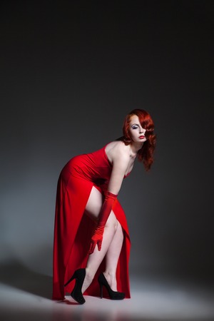 Beautiful young Woman with red hair dressed in red elegant dressの写真素材