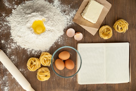 Cooking some tasty food and writing down recipe In open clear note. With ingredients like butter, eggs, flour, pasta.の写真素材