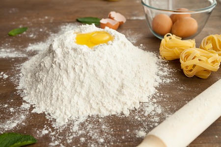 Close up view of cooking dough with fettuccine and eggs nearby with rolling bin in front.の写真素材