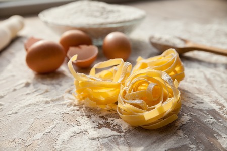 Close up view of fettuccine in cooking process with eggs and flour on background.の写真素材