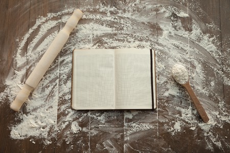 Composition of clear open recipe book in middle and rolling pin with spoon by sides on floured table.の写真素材