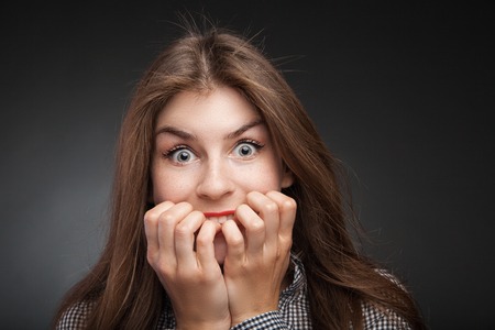 Amazed woman biting nails. Studio headshot on black vignette background.の写真素材