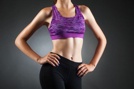 Fit anonymous sport-girl akimbo in black yoga pants and purple top. Studio portrait black background.の写真素材