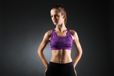Fit sport-girl in black yoga pants and purple top with heat droppings on abdominal muscles. Studio portrait black background.の写真素材