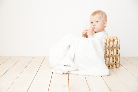 Smiling toddler sitting in bucket with blanket and toy bear looking away on white background.の写真素材