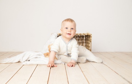 Cheerful toddler in white cloth sitting with blanket and bear smiling at camera on white background.の写真素材