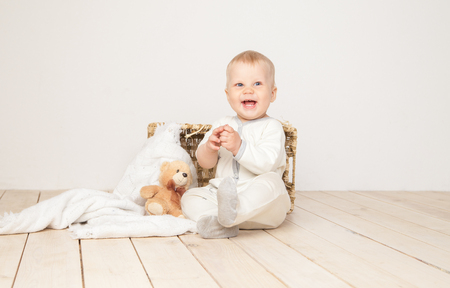 Cheerful toddler in white cloth sitting with blanket and bear smiling at camera on white background.の写真素材