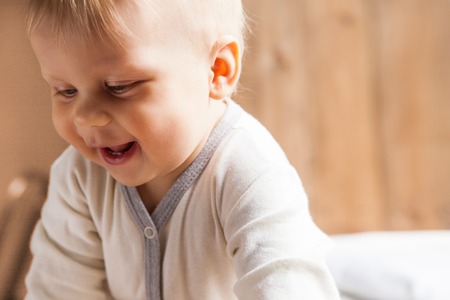 Toddler wearing white cloth looking down and smiling on background of wooden wall.の写真素材