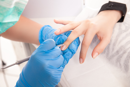 Cropped close up specialist hands making manicure on female hand with special equipment.の写真素材