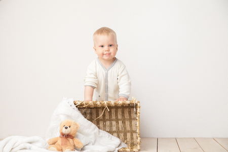 Toddler in white outfit standing and smiling at camera with bucket and bear around on white .の写真素材