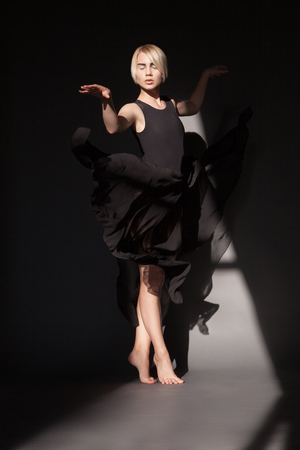 Female in black chiffon dress dancing sensual dance in ray of light on black dark .の写真素材