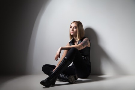 Young trendy girl sitting on floor near wall in pensive pose and looking away.の写真素材