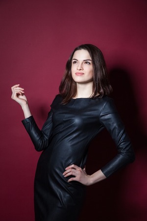 Portrait of young beautiful woman in leather dress on red backgroundの写真素材