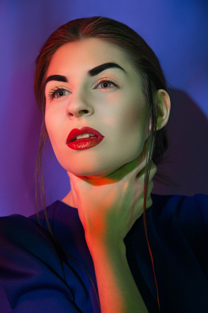 Pretty young woman looking away and holding her neck. Vertical studio shot. の写真素材