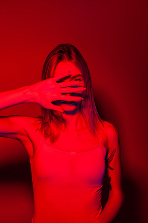 Anonymous woman covering face with hand in red neon lightの写真素材