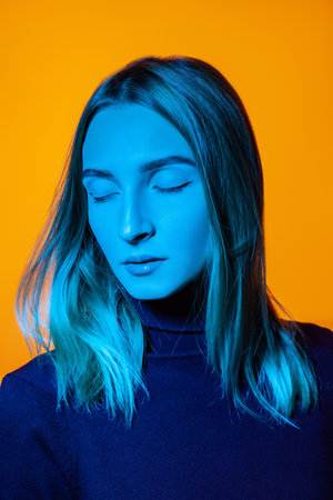 Pensive young woman with closed eyes in bright studio with blue illuminationの写真素材