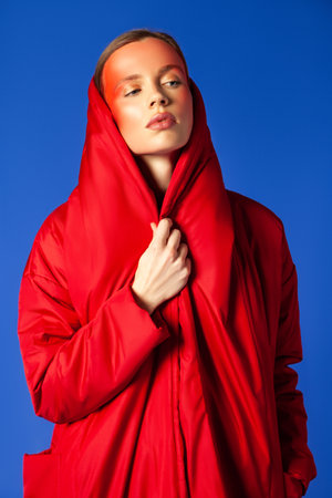 Trendy woman wrapping in red garment against blue backgroundの写真素材